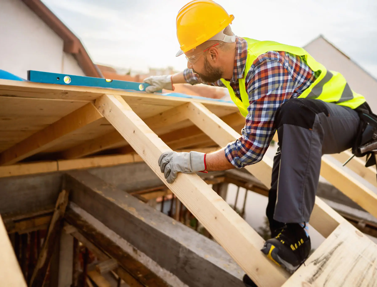 Construction worker measuring wooden roof frame.