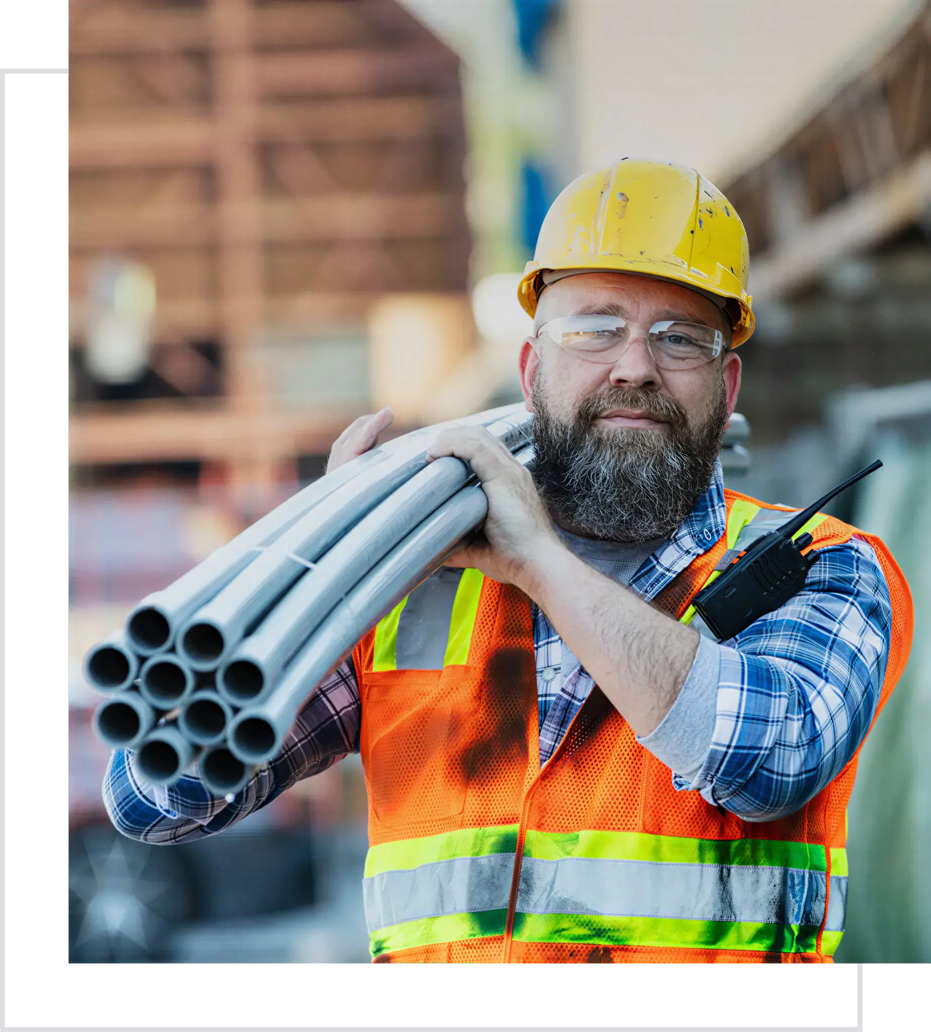 Construction worker carrying pipes, wearing safety gear.